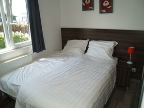 A neatly made bed with white bedding, a wooden headboard, a red bedside lamp, and two wall-mounted flower paintings. - Holiday Home in Dordrecht With Terrace (Dordrecht)