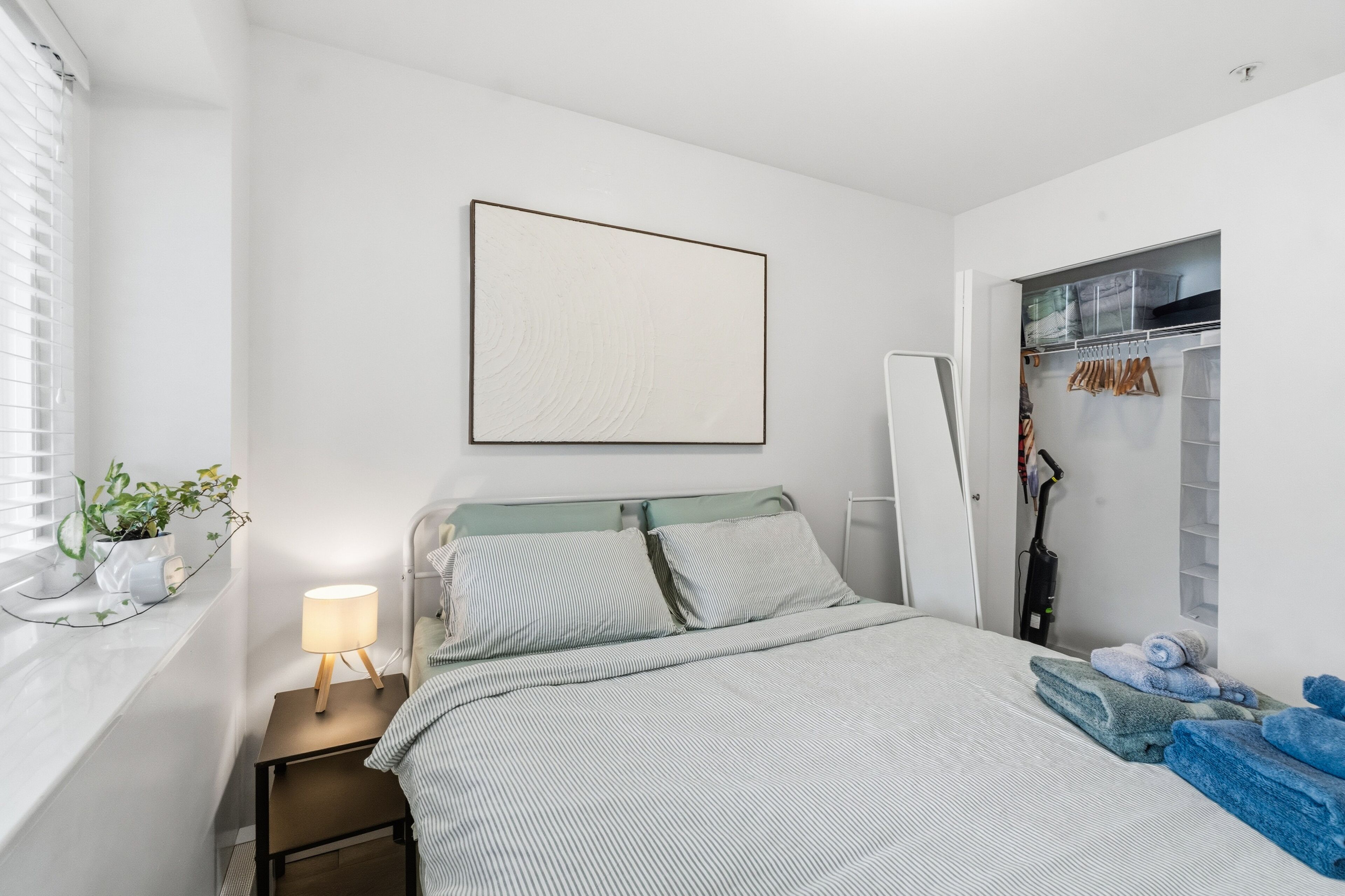 Una camera da letto con un letto, un comodino, una lampada e un armadio pieno di abiti.