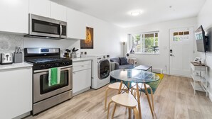 Una cocina moderna con electrodomésticos de acero inoxidable, un comedor con mesa de vidrio y una sala de estar con sofá y televisor.