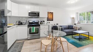 Una cocina moderna con armarios blancos, electrodomésticos de acero inoxidable y un comedor con mesa y sillas de vidrio.