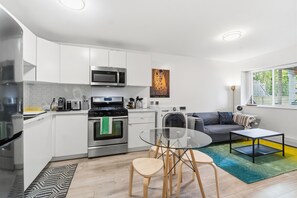 A modern kitchen with white cabinets, stainless steel appliances, and a dining area with a glass table and chairs.