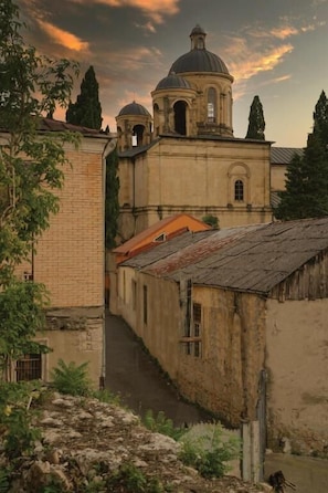A narrow alleyway with a building featuring a dome and bell tower, surrounded by trees and a rustic atmosphere. - DRO Hotel (Kutaisi)