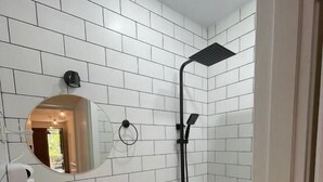 A bathroom with white tiled walls, a sink with a mirror, and a shower. - DRO Hotel (Kutaisi)