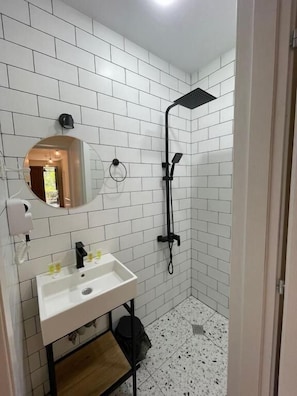 A bathroom with white tiled walls, a sink with a mirror, and a shower. - DRO Hotel (Kutaisi)