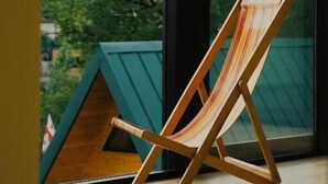 A wooden beach chair with a striped cushion, positioned in front of a large window with a view of green trees. - DRO Hotel (Kutaisi)
