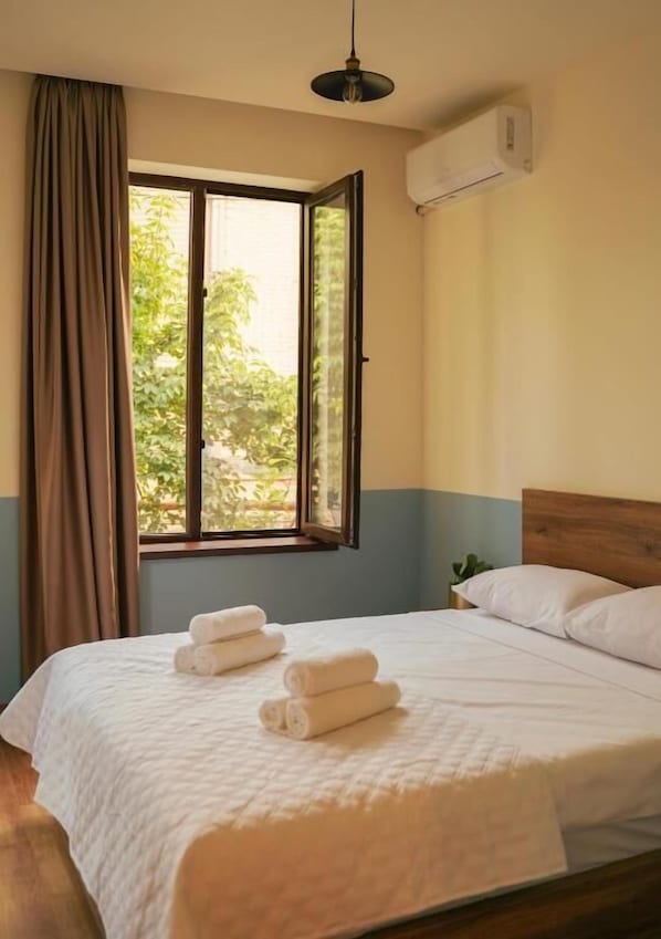 A hotel room with a bed, a window with curtains, and an air conditioning unit. - DRO Hotel (Kutaisi)