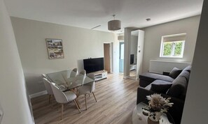 A modern living room with a glass dining table, a sofa, a TV, and a window. - Stable Cottage - with free parking! (Woodborough)