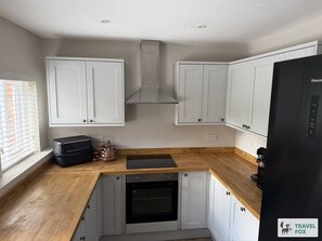 Une cuisine compacte avec des meubles blancs, un four encastré, une plaque de cuisson à induction noire et un réfrigérateur noir.