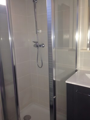 Une salle de bain moderne avec une douche à parois de verre, un mur recouvert de carreaux blancs et un lavabo noir.