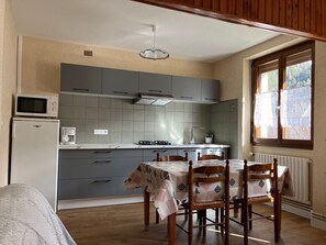 Une cuisine de taille réduite avec des meubles gris, un four à micro-ondes et une table avec des chaises.