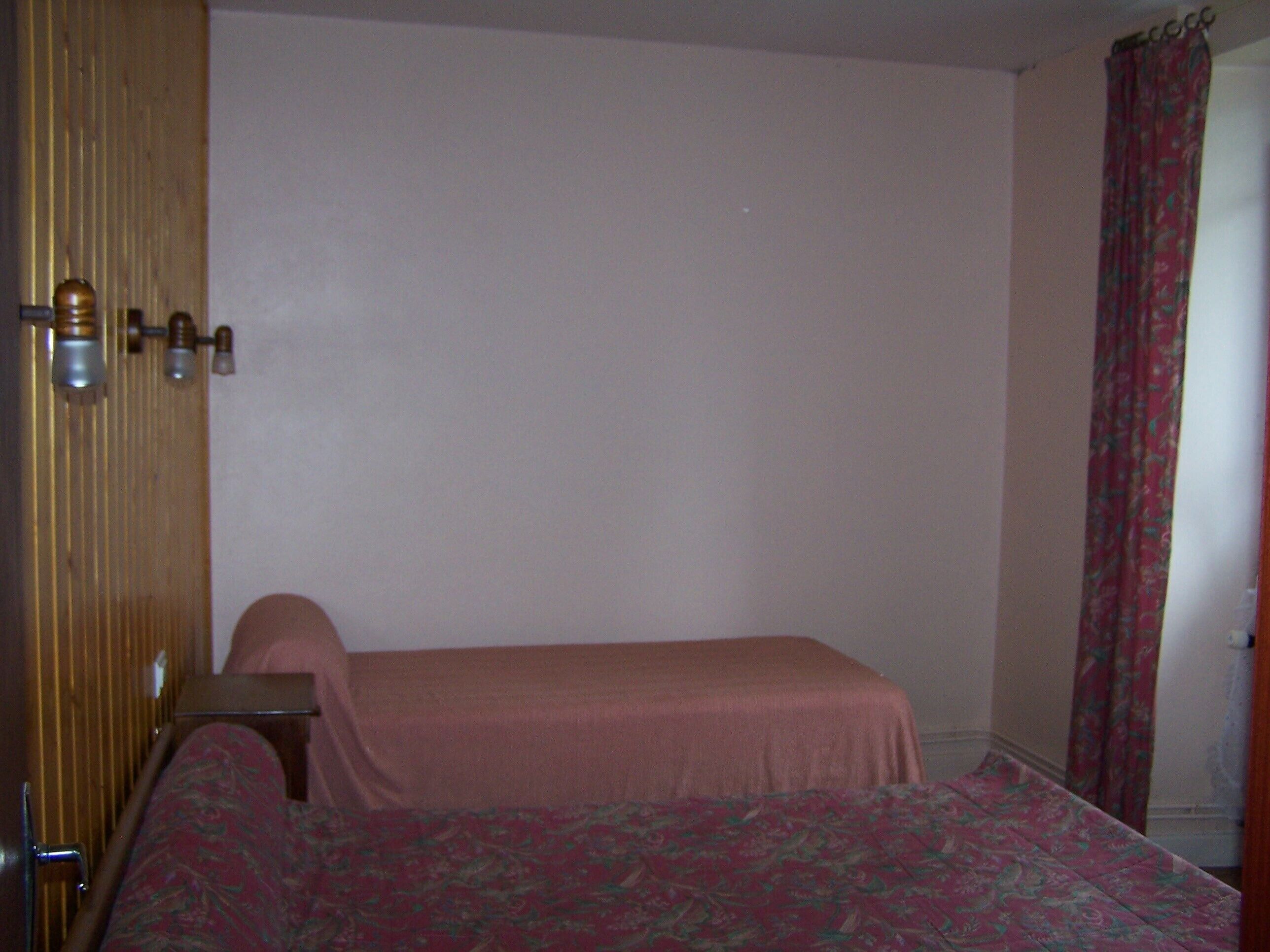 Una stanza con un letto, una porta in legno e una tenda.