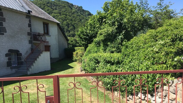 Una casa con una escalera que lleva a una puerta, rodeada de abundante vegetación y un paisaje montañoso.