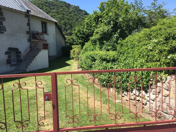 Une maison avec un escalier menant à une porte, entourée d’une végétation luxuriante et avec une chaîne de montagnes en arrière-plan.