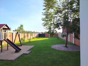 A fenced backyard with a playground, a grassy area, and a paved path. - 5 Guest House Spacious: Quincho Swimming Pool Games (San Bernardino)
