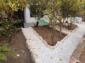 Un chemin de pierres qui traverse un jardin planté d’arbres et où est installé un hamac.