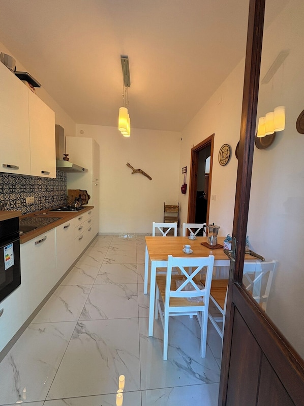 Une cuisine avec des meubles blancs, un plan de travail en bois et un coin repas comprenant des chaises blanches et une table en bois.