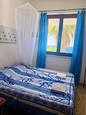 Une chambre avec un lit, une fenêtre ornée de rideaux bleus, un baldaquin blanc et une couvre-lit à motifs.