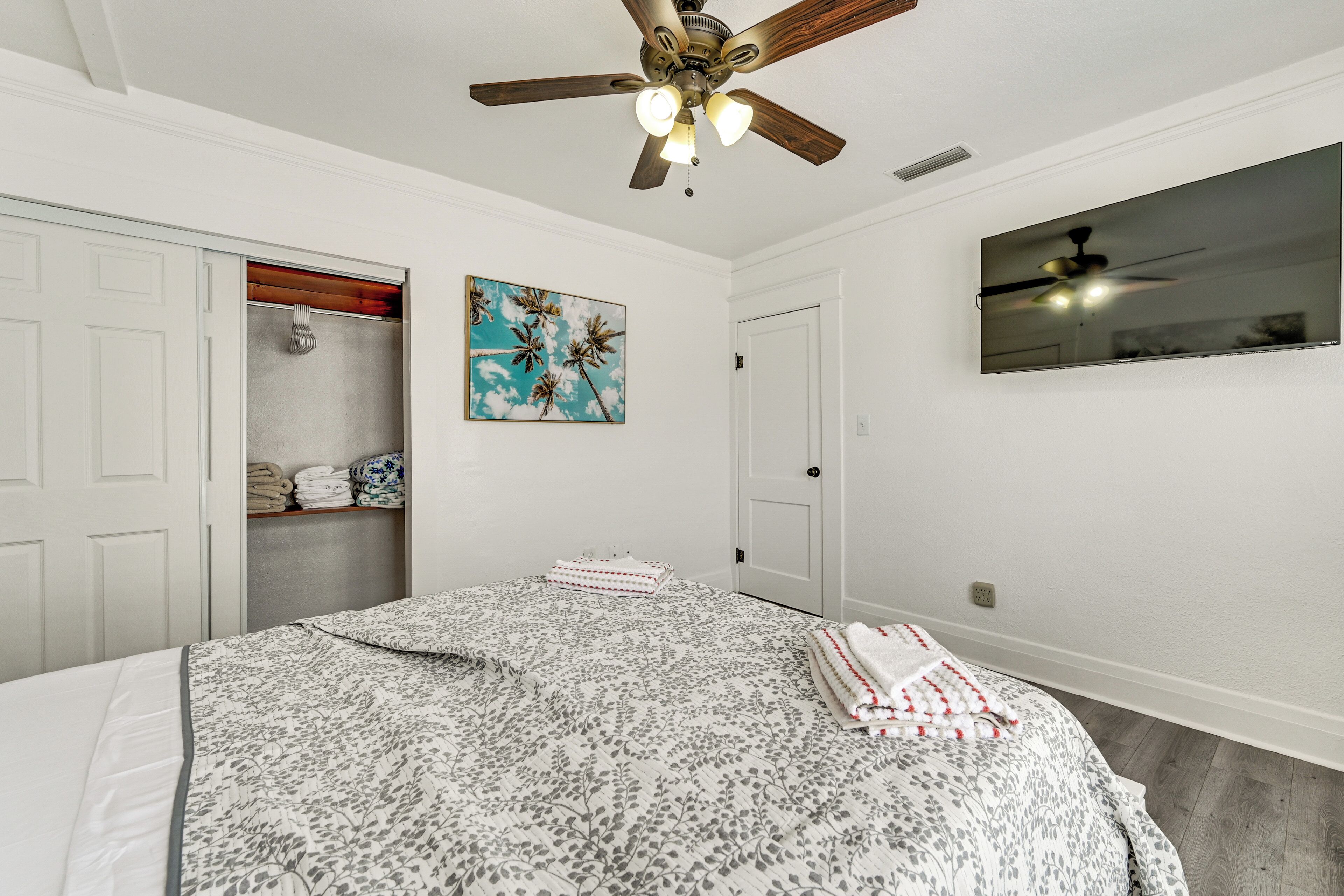 Ein Schlafzimmer mit Bett, Deckenventilator, Kleiderschrank, einem Gemälde und einem Spiegel.