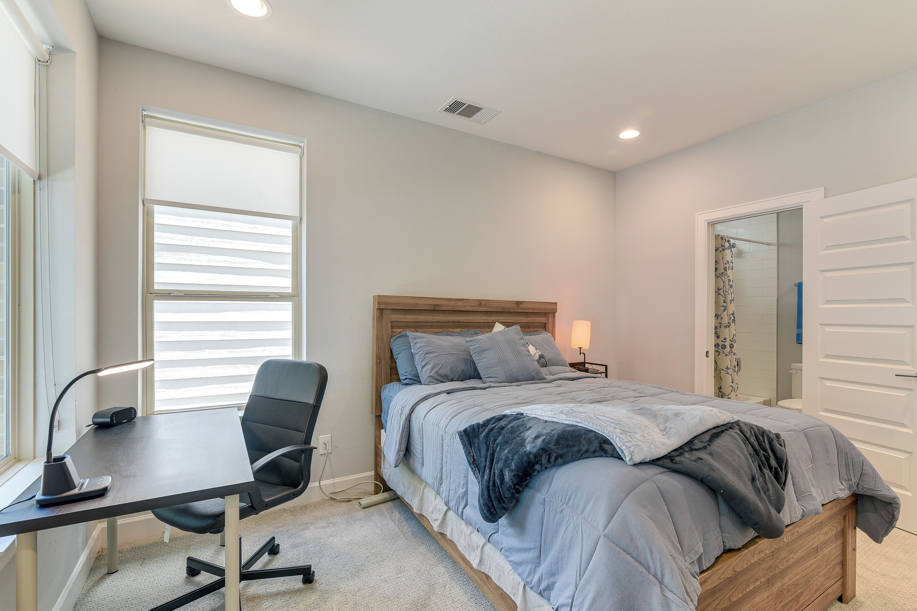 A bedroom with a bed, desk, chair, and a window with blinds.