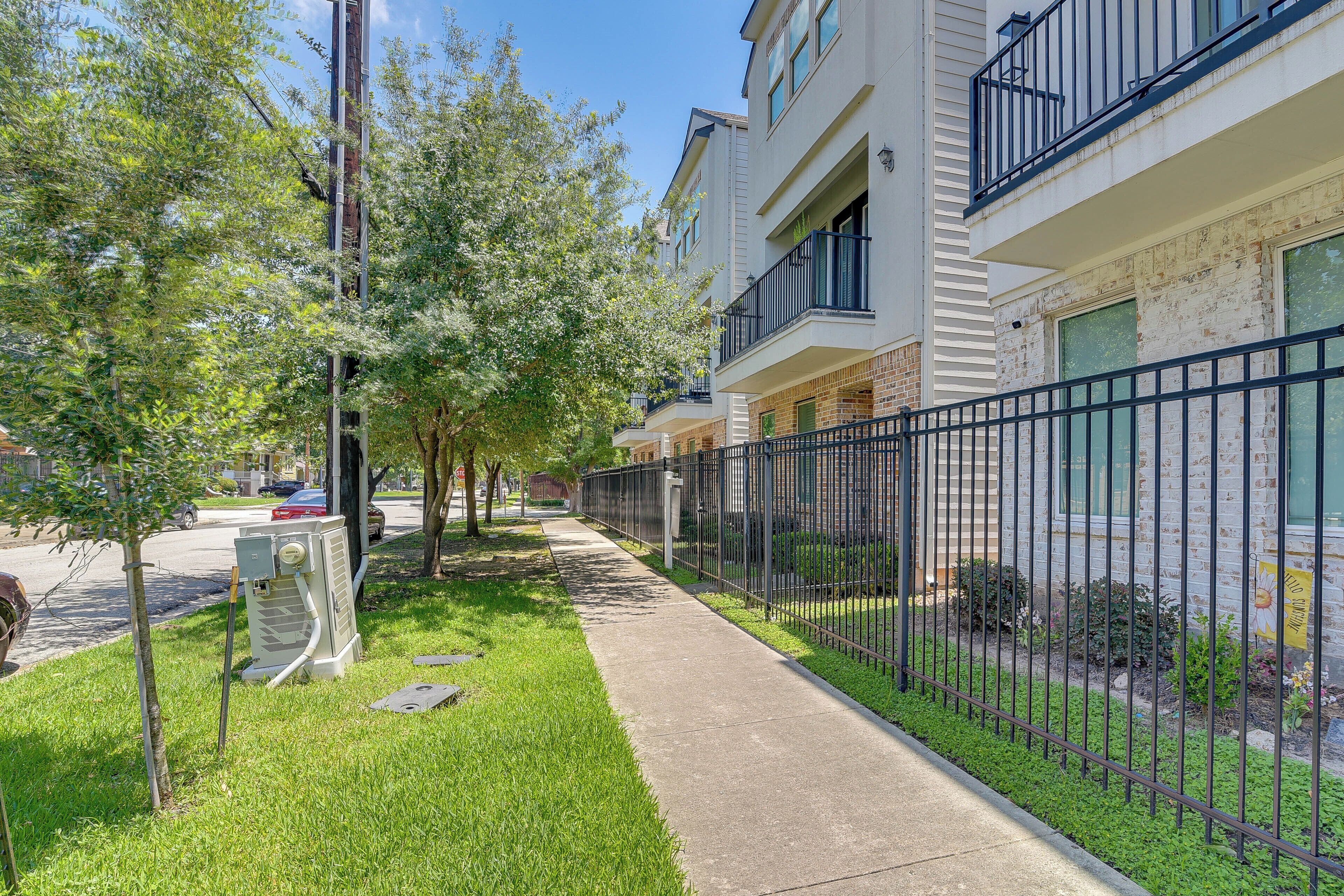 A residential building with a sidewalk, a fenced area, and a tree.