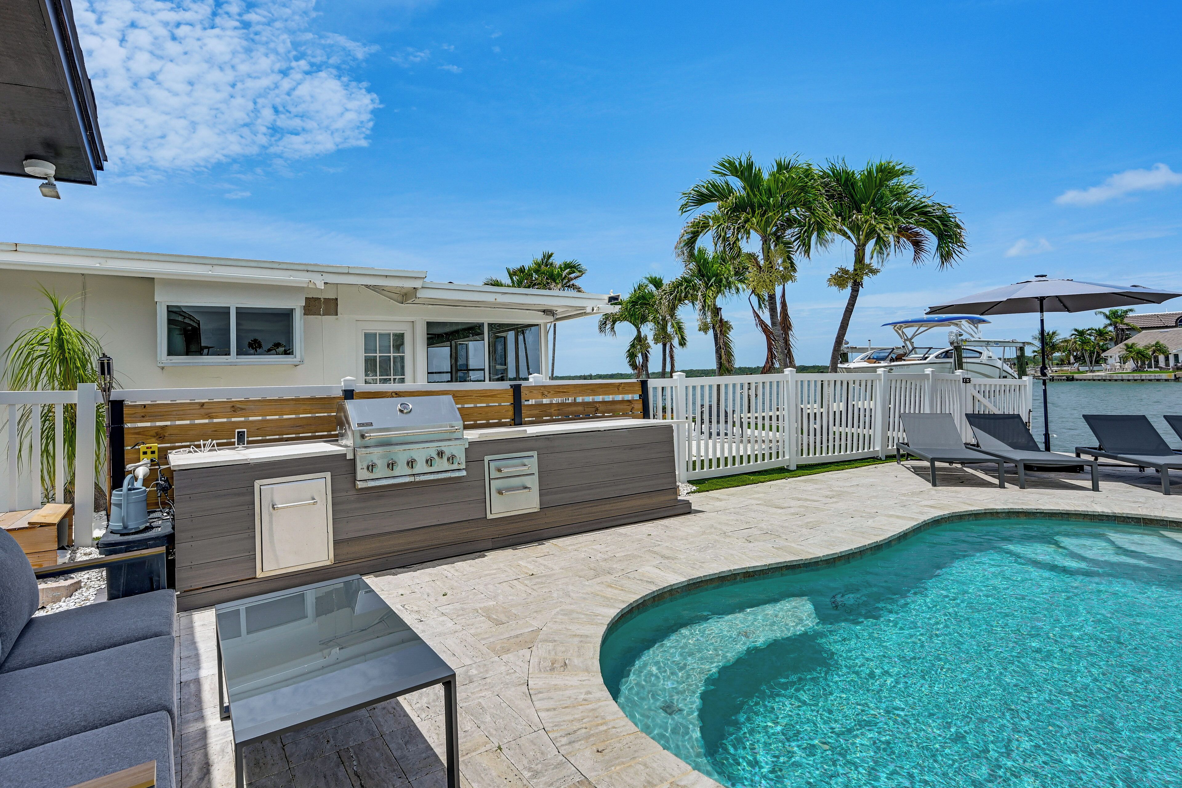 A backyard with a swimming pool, a barbecue area, and lounge chairs.