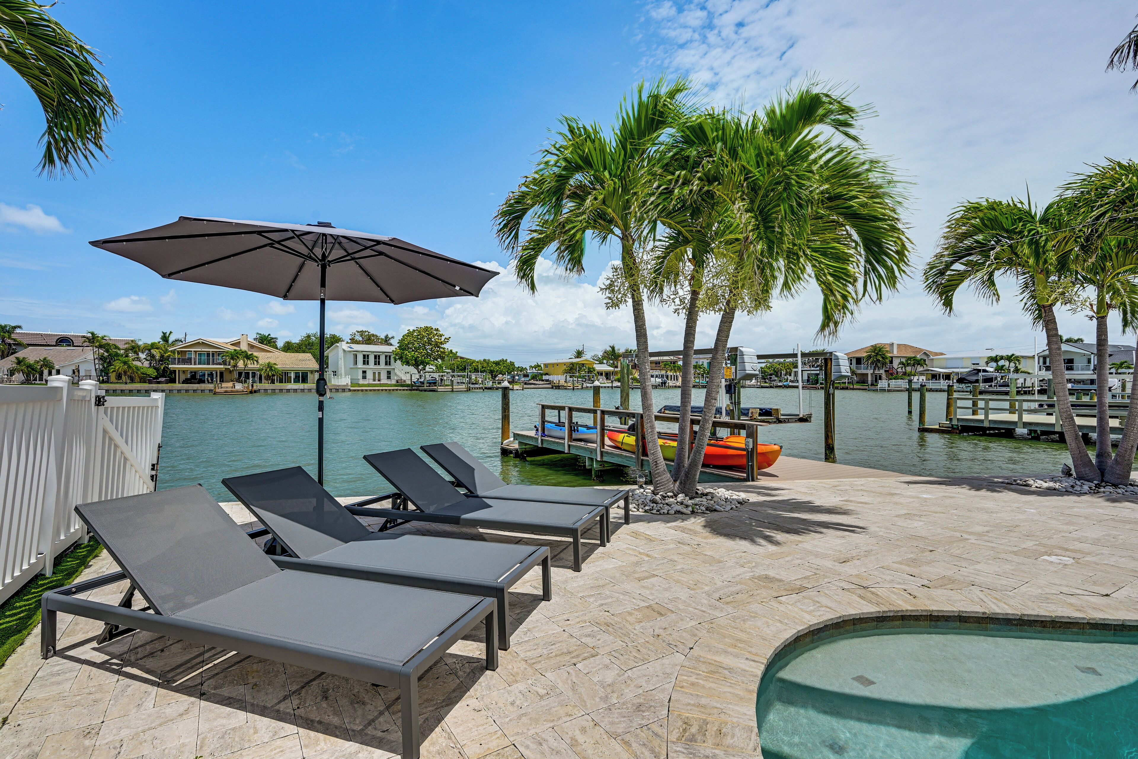 A poolside area with lounge chairs, an umbrella, and a view of the water.