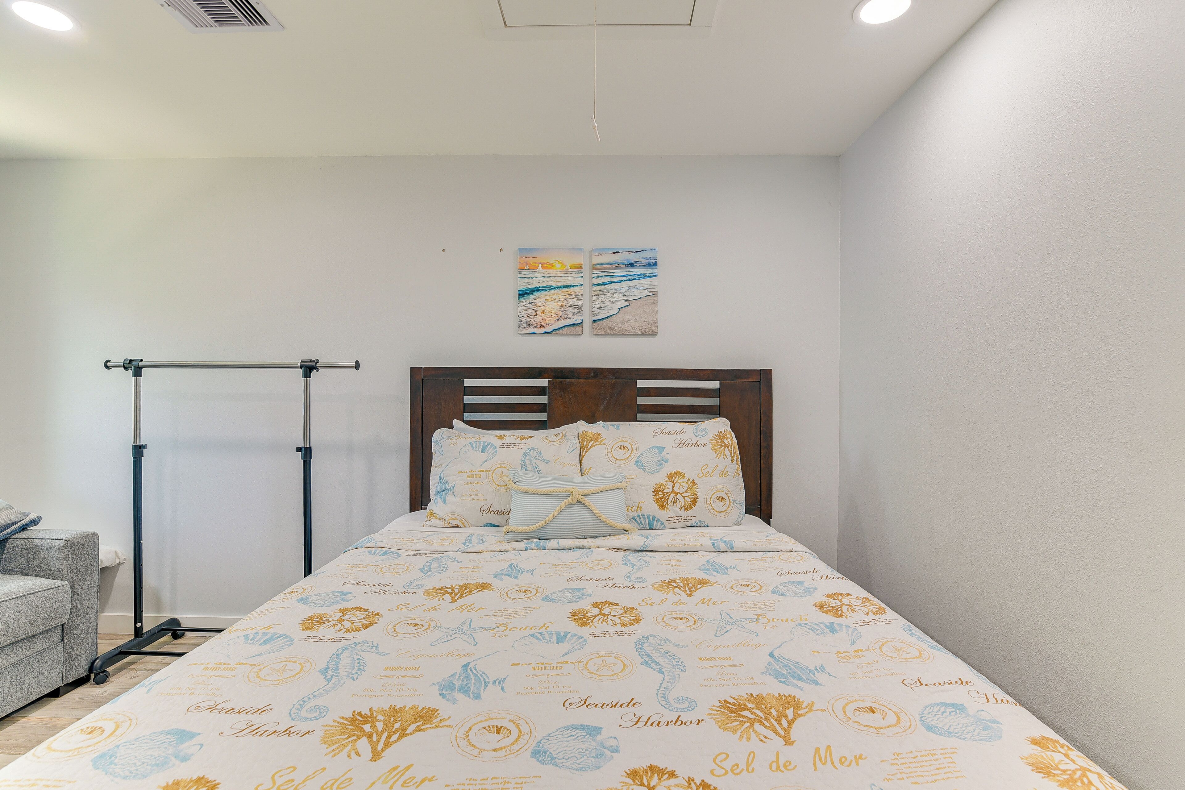 Cama bem arrumada com colcha estampada, cabeceira de madeira e uma obra de arte pendurada na parede.