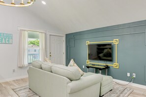 A living room with a sofa, a television mounted on the wall, a door, and a window with curtains. - 1 Mi to Beach & Bay! Group Getaway in Galveston (Galveston)