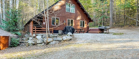 A cabin with a stone foundation, wooden deck, and a covered grill area.