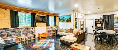 A cozy living room with a leather couch, a bookshelf, a coffee table, and a dining area with a table and chairs.