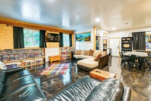 A cozy living room with a leather couch, a bookshelf, a coffee table, and a dining area with a table and chairs. - Group Escape w/ Hot Tub, 18 Mi to Bavarian Village (Leavenworth)