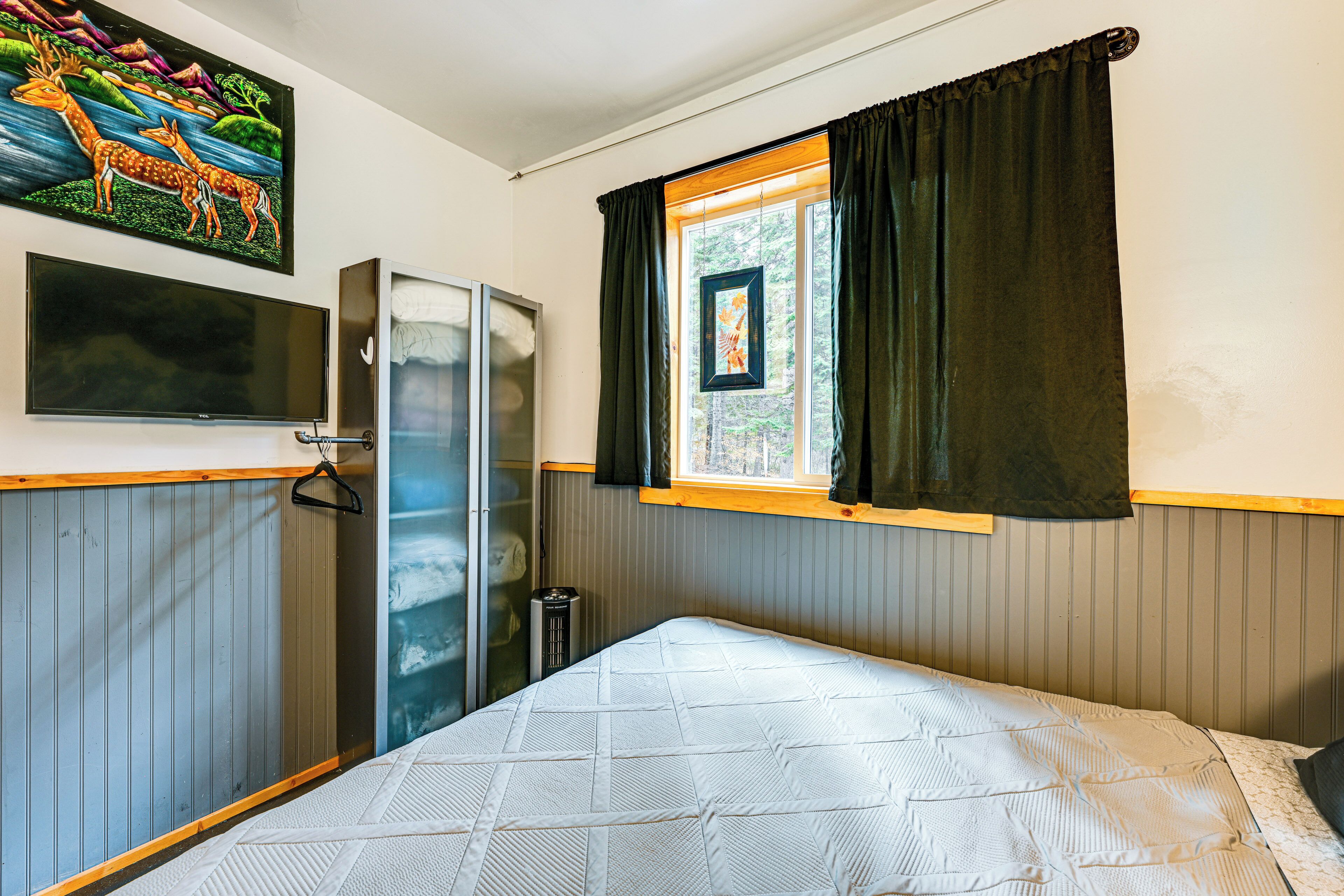 Une chambre avec un lit, une télévision, une armoire et une fenêtre avec des rideaux.