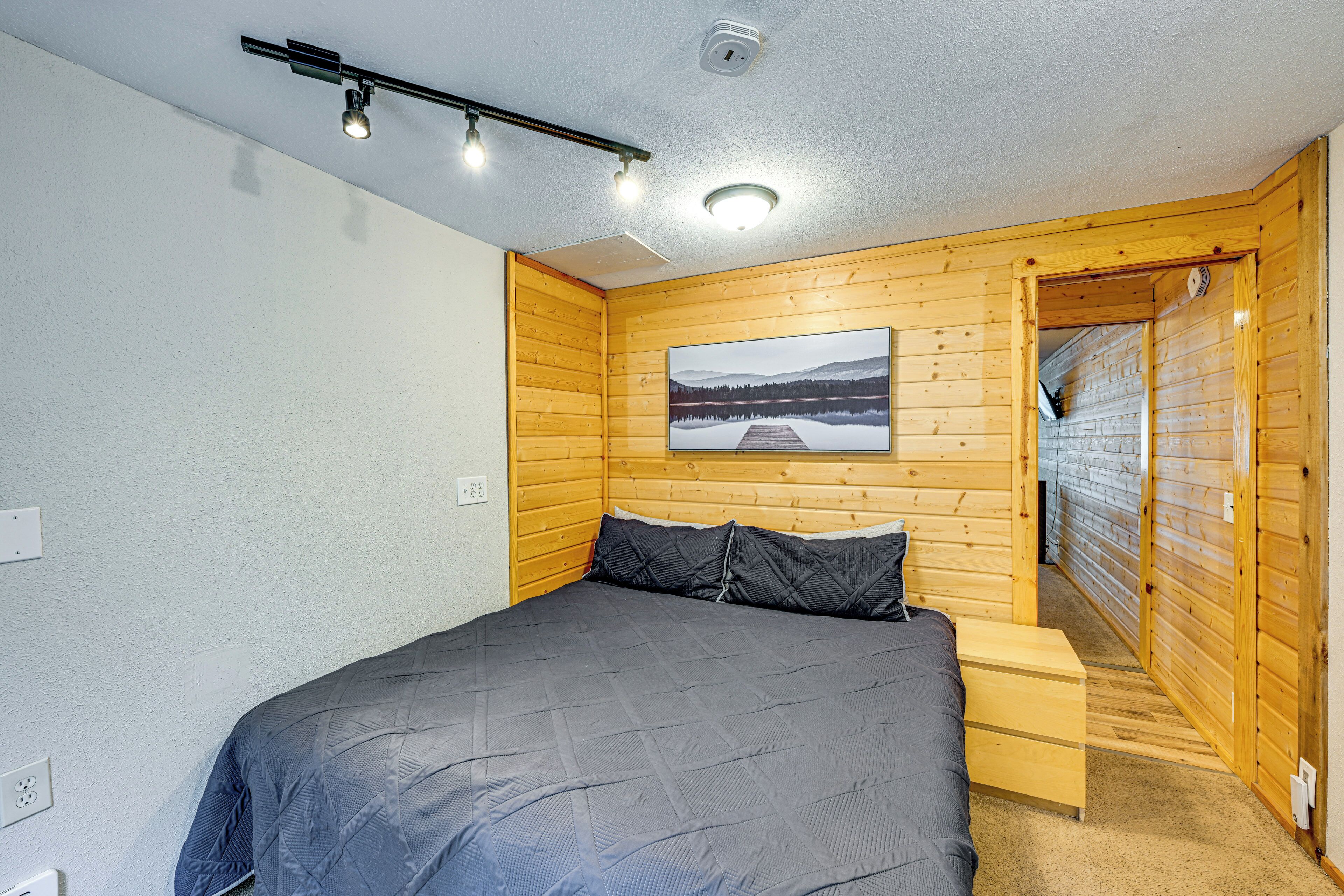 A bedroom with a bed, a nightstand, a wooden wall with a picture, and a door leading to another room.