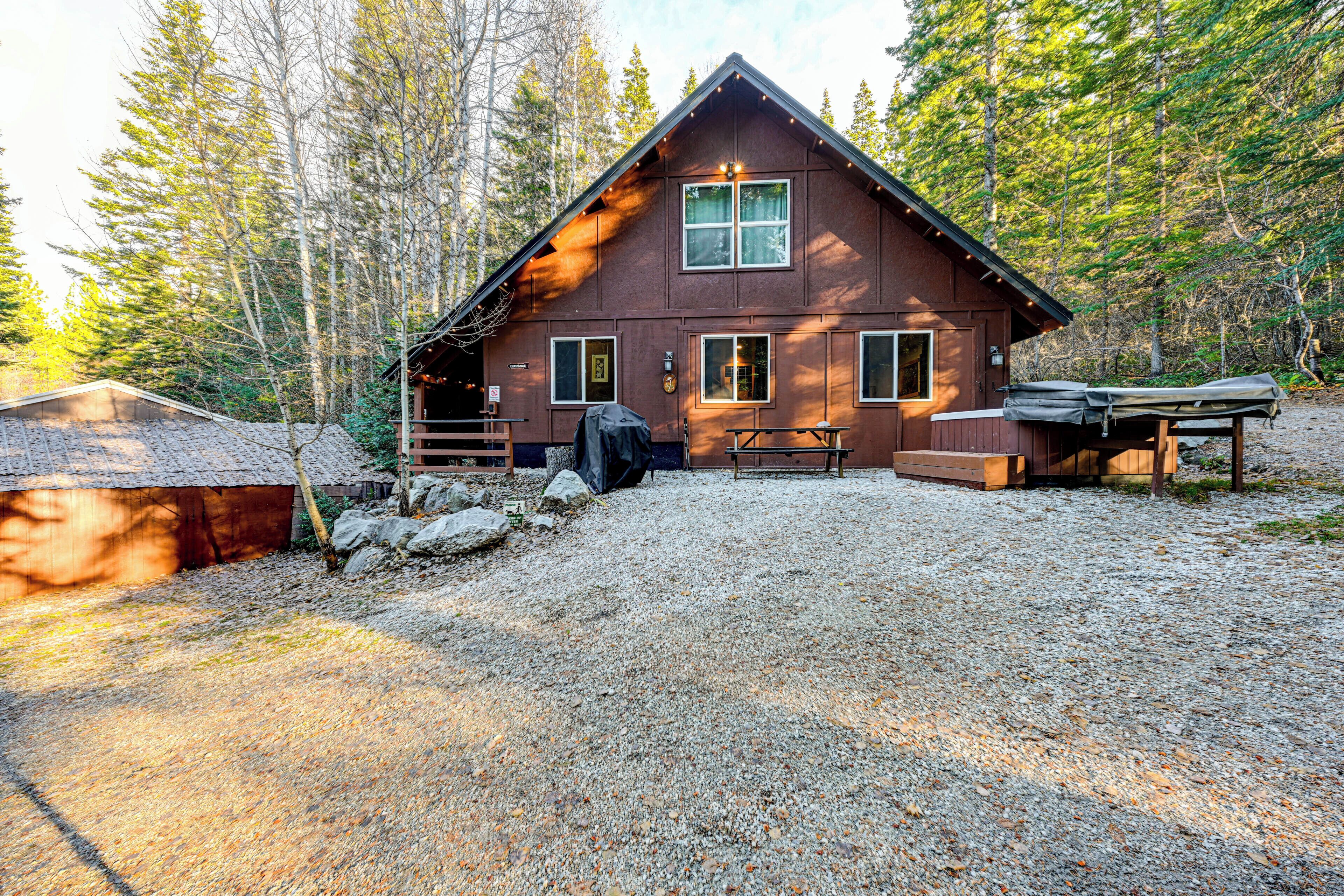 A cabin with a gravel driveway, a covered picnic table, and a grill.