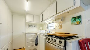 A compact kitchen with white cabinets, a stove, a window, and a 'RELAX' sign. - Heated Pool, Games & Socials! Zephyrhills Home (Zephyrhills)