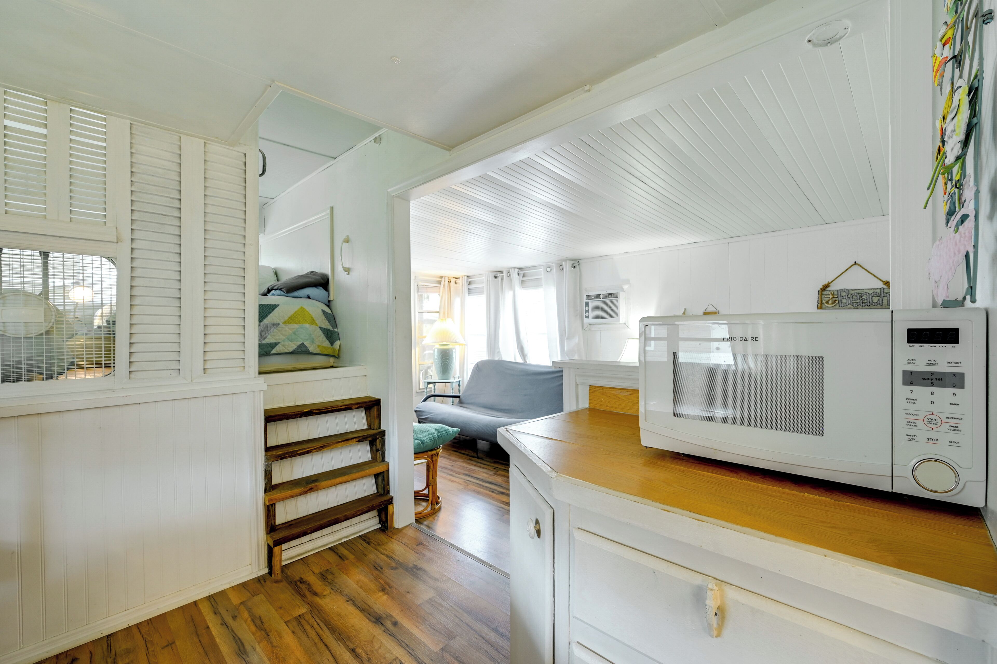 A compact kitchen with a microwave, wooden flooring, and a small seating area with a sofa and cushions.