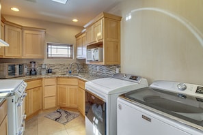 A kitchen with wooden cabinets, a microwave, a coffee maker, a stove, and a washing machine.