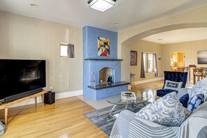A living room with a flat-screen TV, a fireplace, a sofa, and a dining area in the background.
