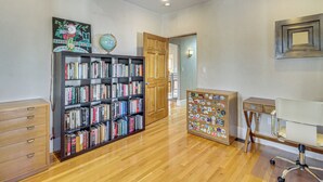 A room with a wooden bookshelf, a desk with a chair, and a door leading to another room. - Walkable Home w/ Office in Downtown Albuquerque! (Albuquerque)