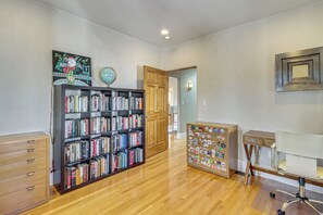 Ein Zimmer mit einem hölzernen Bücherregal, einem Schreibtisch mit Stuhl und einer Tür zu einem weiteren Raum.