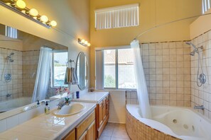 Une salle de bain avec une baignoire, deux lavabos, un grand miroir et une fenêtre avec des rideaux.