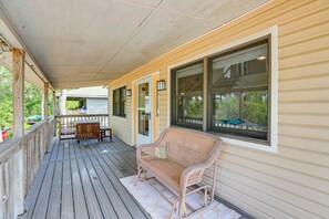 A covered porch with a wicker sofa, wooden table, and chairs.