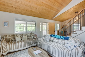 A living room with a wooden ceiling, a sofa with patterned cushions, a coffee table, and a staircase.