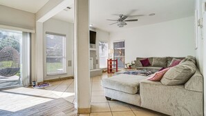 A spacious living room with a large sofa, a ceiling fan, and a view through a sliding glass door to the outdoors. - Arlington Home: Pool Oasis Near At&t Stadium (Grand Prairie)