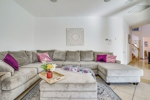 A living room with a sectional sofa, a coffee table with a tray, and a decorative wall piece. - Arlington Home: Pool Oasis Near At&t Stadium (Grand Prairie)