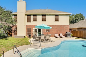 A residential backyard with a swimming pool, patio furniture, and a brick house.