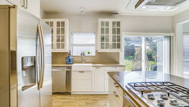 A modern kitchen with a stainless steel refrigerator, white cabinets, a gas stove, and a window overlooking a backyard. - Arlington Home: Pool Oasis Near At&t Stadium (Grand Prairie)