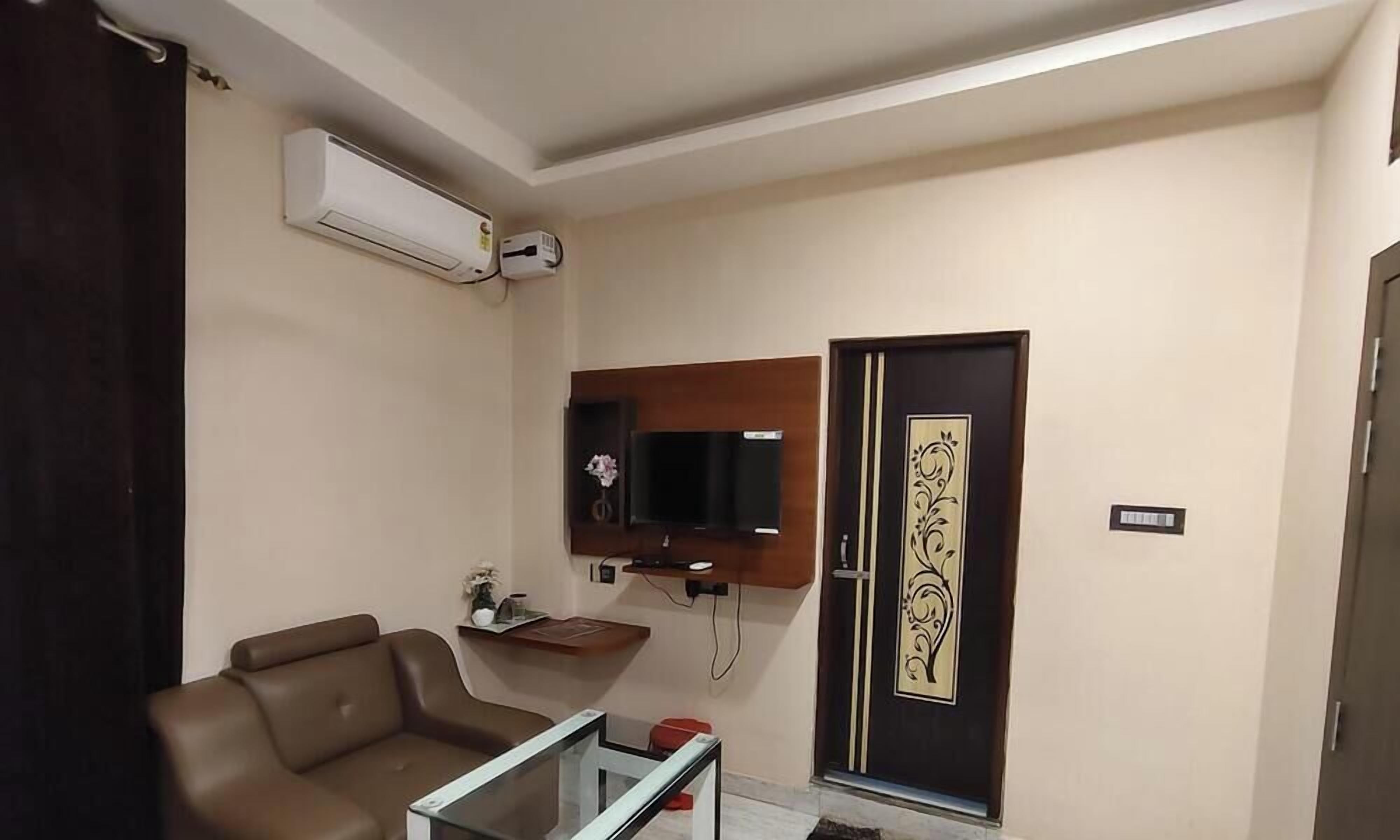 Una sala de estar con un sofá, un televisor fijado a la pared, una mesita y una puerta decorativa.