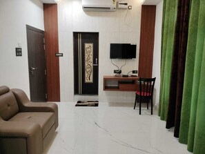 A room with a sofa, a desk with a chair, a television, and a door with a decorative panel.