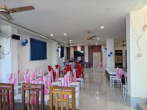 A spacious indoor area with ceiling fans, a flat-screen TV, and rows of tables and chairs.
